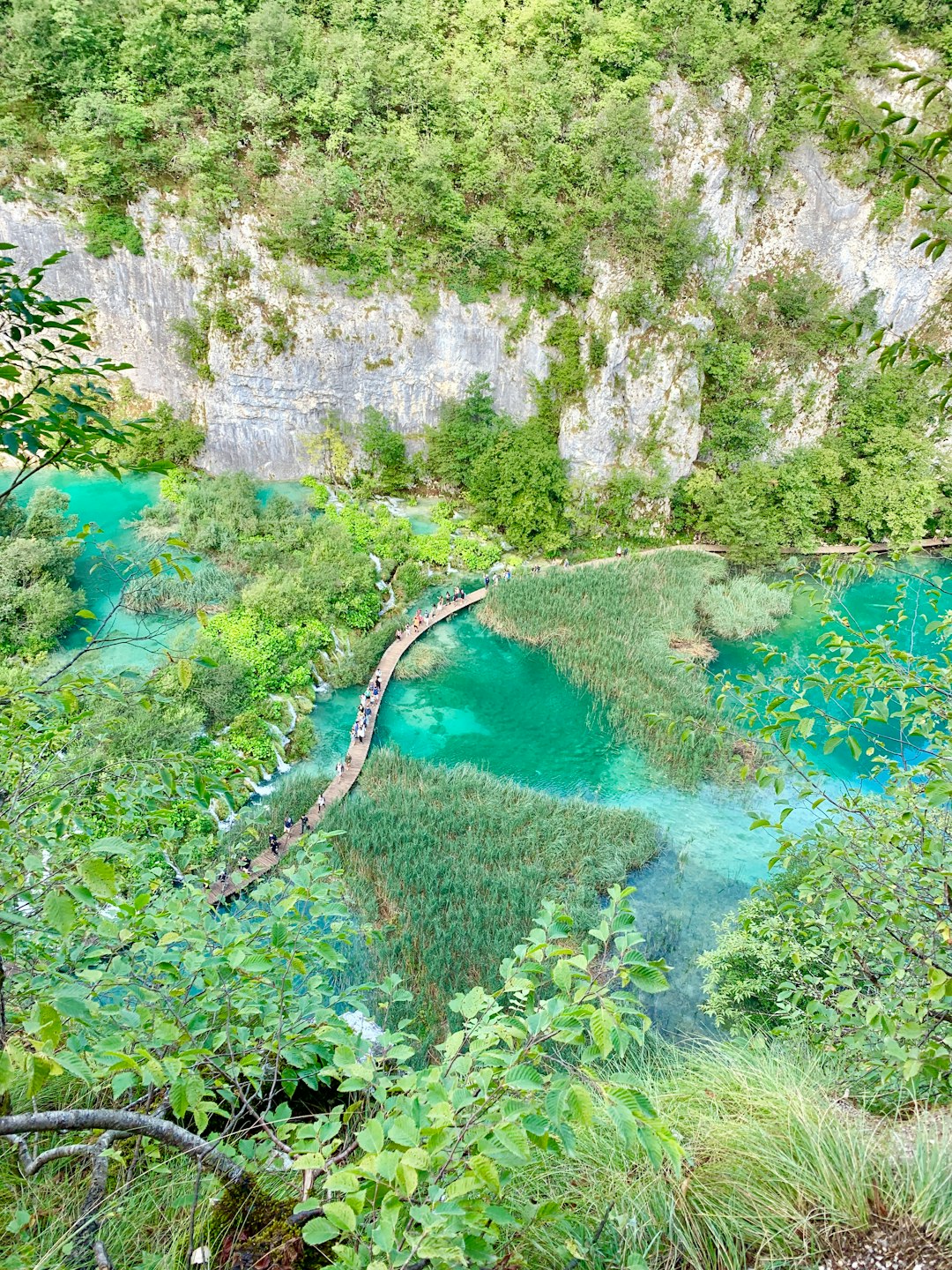 Visitors walking on boardwalk over turquoise water at Plitvice Lakes